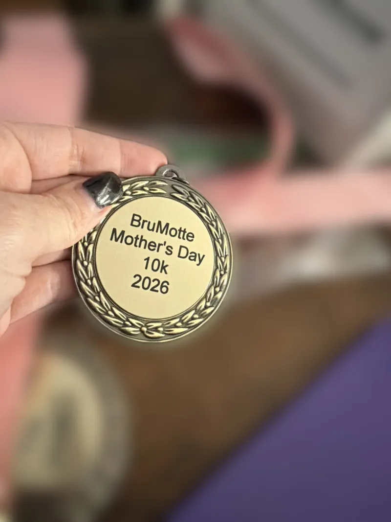 An engraved event medal with a pink neck ribbon.